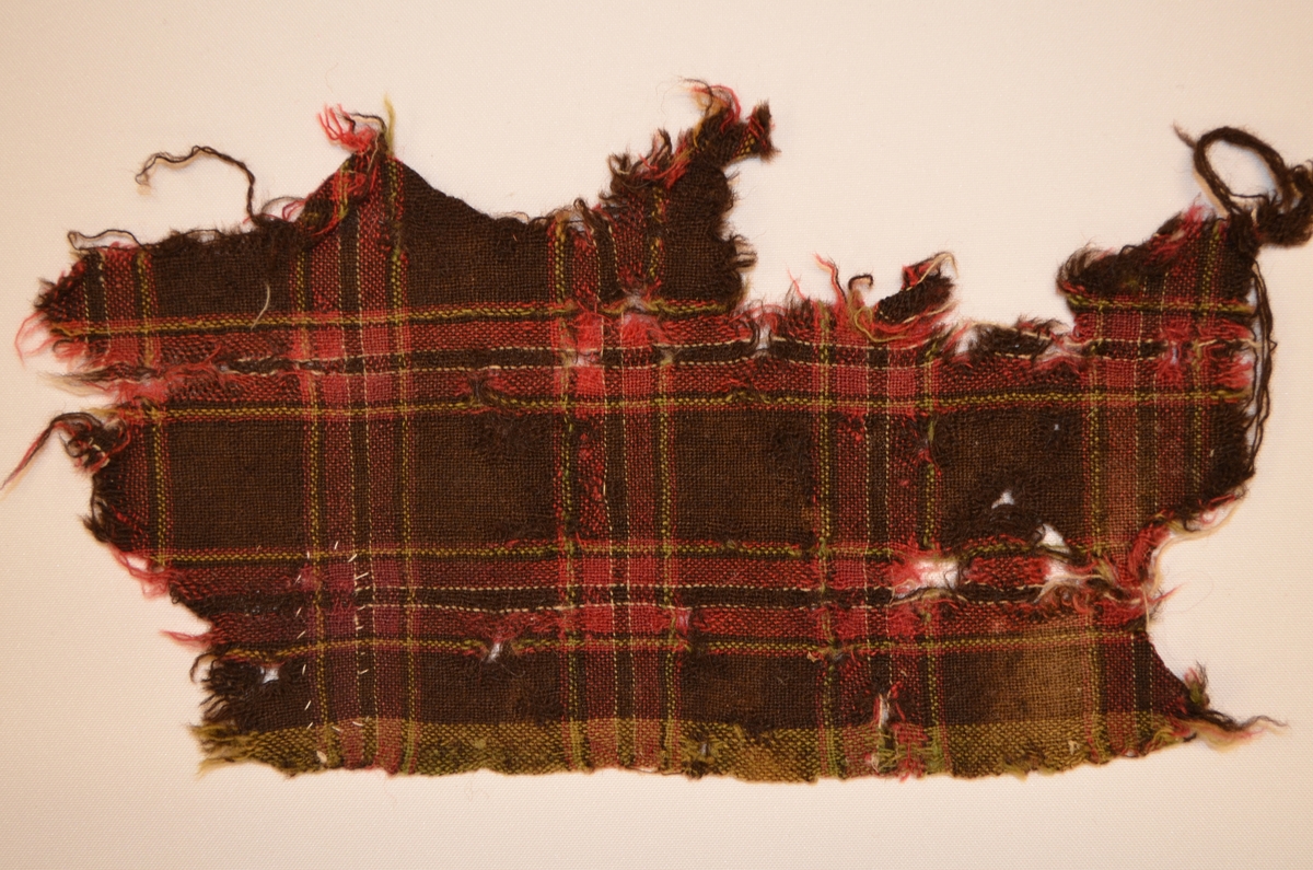 Stoffbit i ull, rutete i sauebrunt, raudrosa, kvitt grønt.