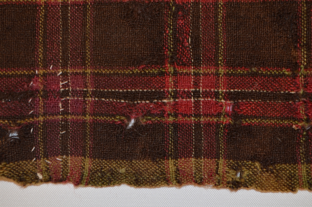 Stoffbit i ull, rutete i sauebrunt, raudrosa, kvitt grønt.