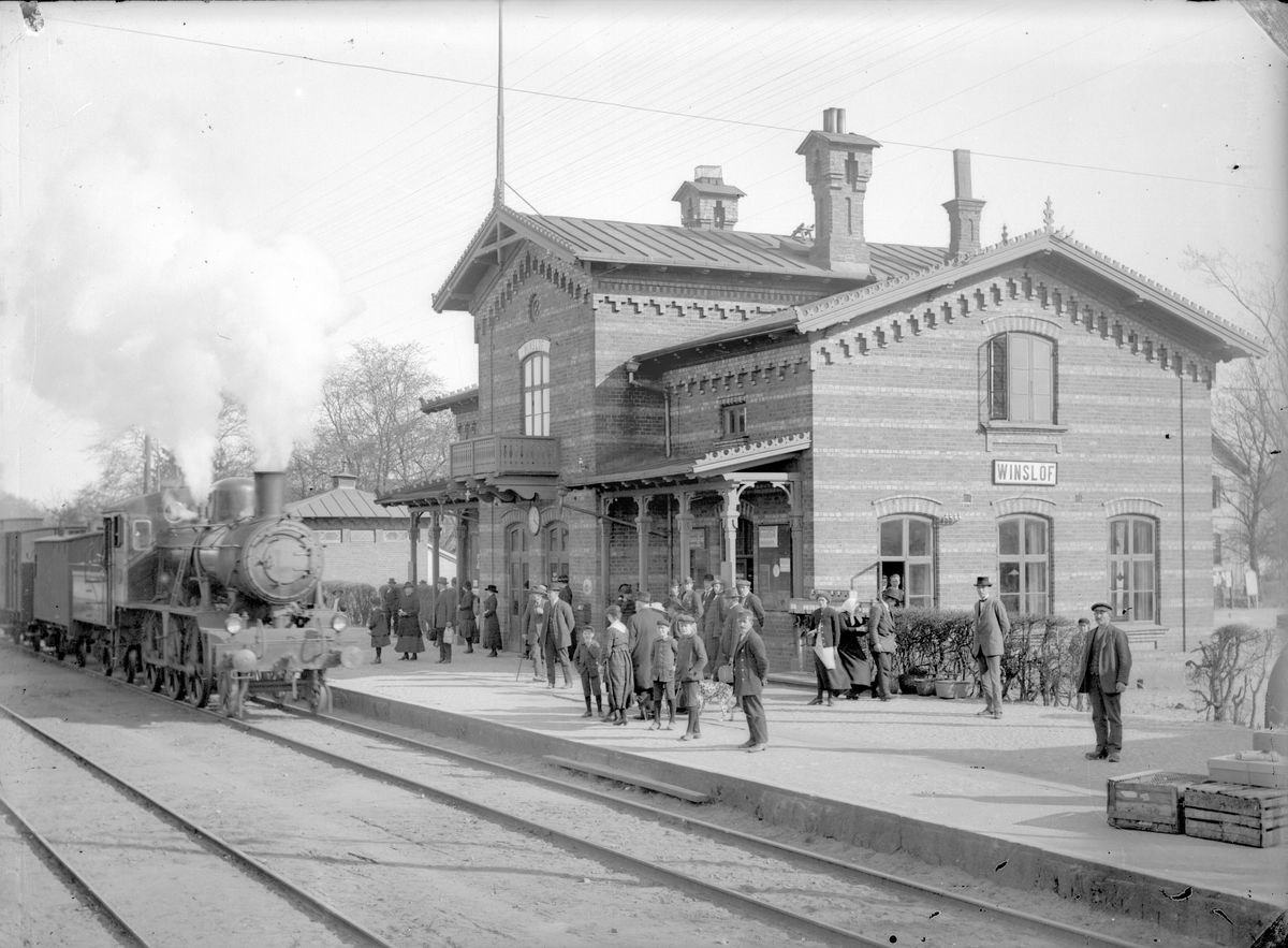 Stationen. Ångtåg inne på stationen. Resande på plattformen.