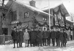 Personal framför Avesta station. Stationen dekorerad för statsinvigningen. Stationföreståndare Wictor Roslund stående längst fram i mitten.