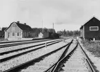 Näs Bruk station där står ett tåg på väg bort. Till höger en lastplats.