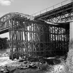 Broarbete vid Skellefteåälven, Kusfors. Järnvägsbron byggdes med en kombination av stående och hängande parabelfackverk. År 1943 hade den ursprungliga bron, som togs i bruk 1893, tjänat ut. Då byttes de tre stålspannen ut mot nya medan samma landfästen och brostöd användes. Den nya bron hade underliggande stålbalkar i alla tre spann. Det långa mittspannet var dessutom utformat som en bågbro med vertikala stag ned till den underliggande balken. Bron trafikerades fram till linjeomläggningen 1993.