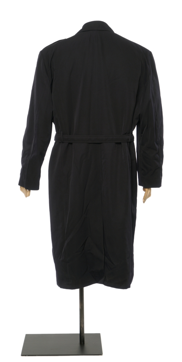 Mørkblå kappe dobbelspent med fire knapper med riksløve-motiv. Epauletter uten tilsatt distinktsjoner. Split i bak, og innebygd belte med sammenlåsende lukking. Avtagbar vattert foder festet av glidelåser rundt inner kanten. Stoffet er finveved kypert blanding av ull og polyester) Jakke er foda med syntetisk sort stoff. Tekstil merke på venstre arm, riksløve med hvit øks omgitt av eikeblader over TOLL.