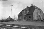 Stationen. Mitt för stationshuset står en semafor med så kallade gallerverksvingar. Signalen visar stopp.