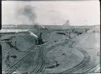 Malmupplag i Luleå station. 1888-03-12  det första malmtåget kom ned till Luleå. Stationshuset färdigtbyggdes 1887. Exploateringen i malmgruvorna började öka. Kapaciteten har successivt också ökat genom förstärkning av bana, broar, mötesstationer och elektrisk drift. Malmbanan byggdes av Sverige & Norges Järnväg. Ångdriven kran.