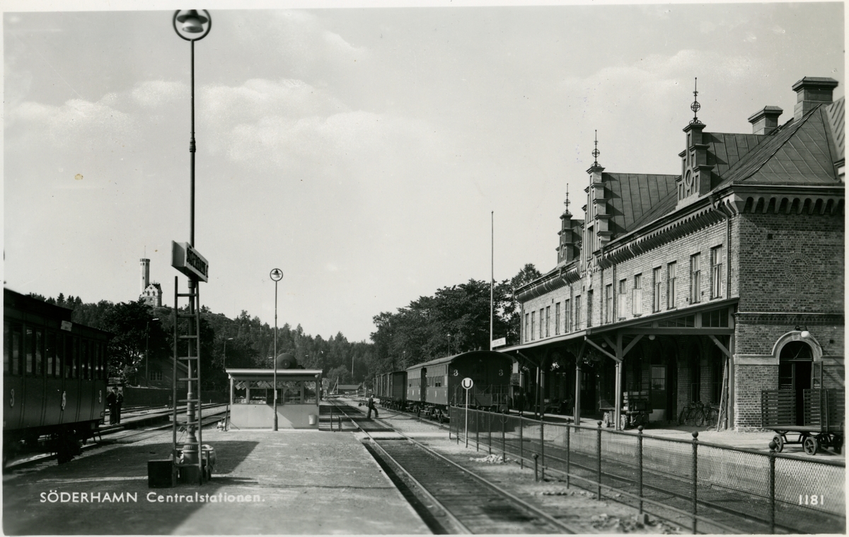 Söderhamn station.
Till vänster en Statens Järnvägar, SJ C3a och de två vagnarna till höger så kallade "lejonburar" litt SJ C4. Bakom kiosken skymtar en gasvagn SJ Q4 från vilket leder en slang över spåren till C4-vagnarna. En av dessa får vid tillfället oljegas till belysningen påfyllt från Q4-vagnen.
TT