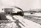 Invigningståget framför det flaggprydda stationshuset i Hedemora 8/11 1880.
Frampå loket sitter en krönt sköld med korslagda dalpilar på.