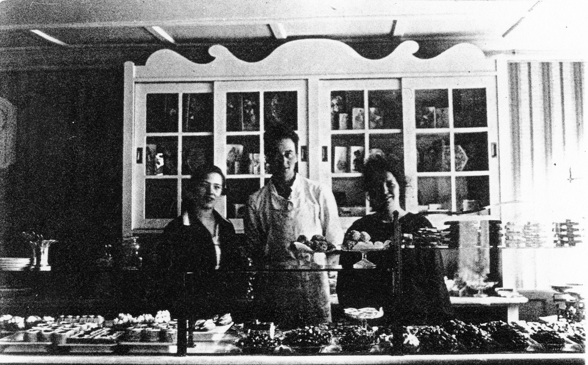 Bild tagen inifrån Ljungblads konditori. Bakom disken, med ett stort urval av konfektyrer, står 2 kvinnor och 1 man. 
Från vänster möjligen Judit Ljungblad, gift med Axel Ljungblad, född Andersson.