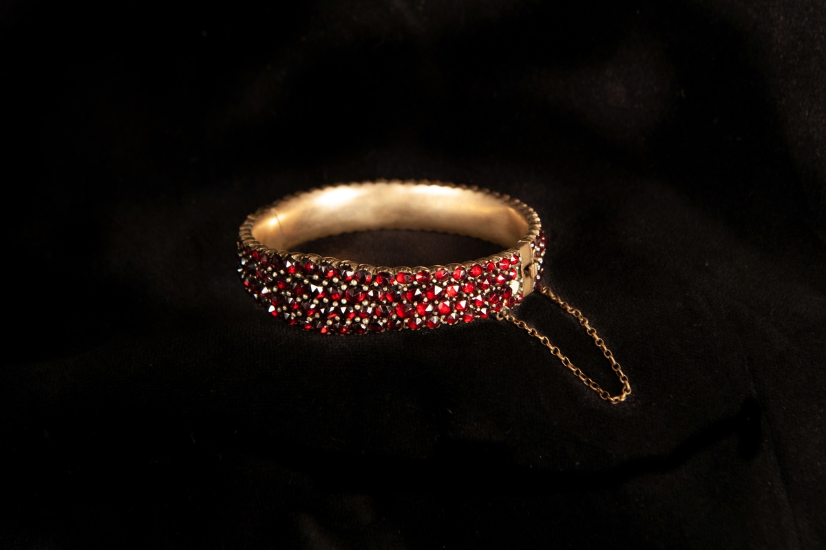 Ett armband, tätt besatt med slipade röda granater. Infattade i förgylld metall, troligen silver. Armbandet något avsmalnande åt sidorna.Smycket ligger i specialgjord svart, ask med röd sammet invändigt och ett snäpplås. 
Inga stämplar på armbandet.