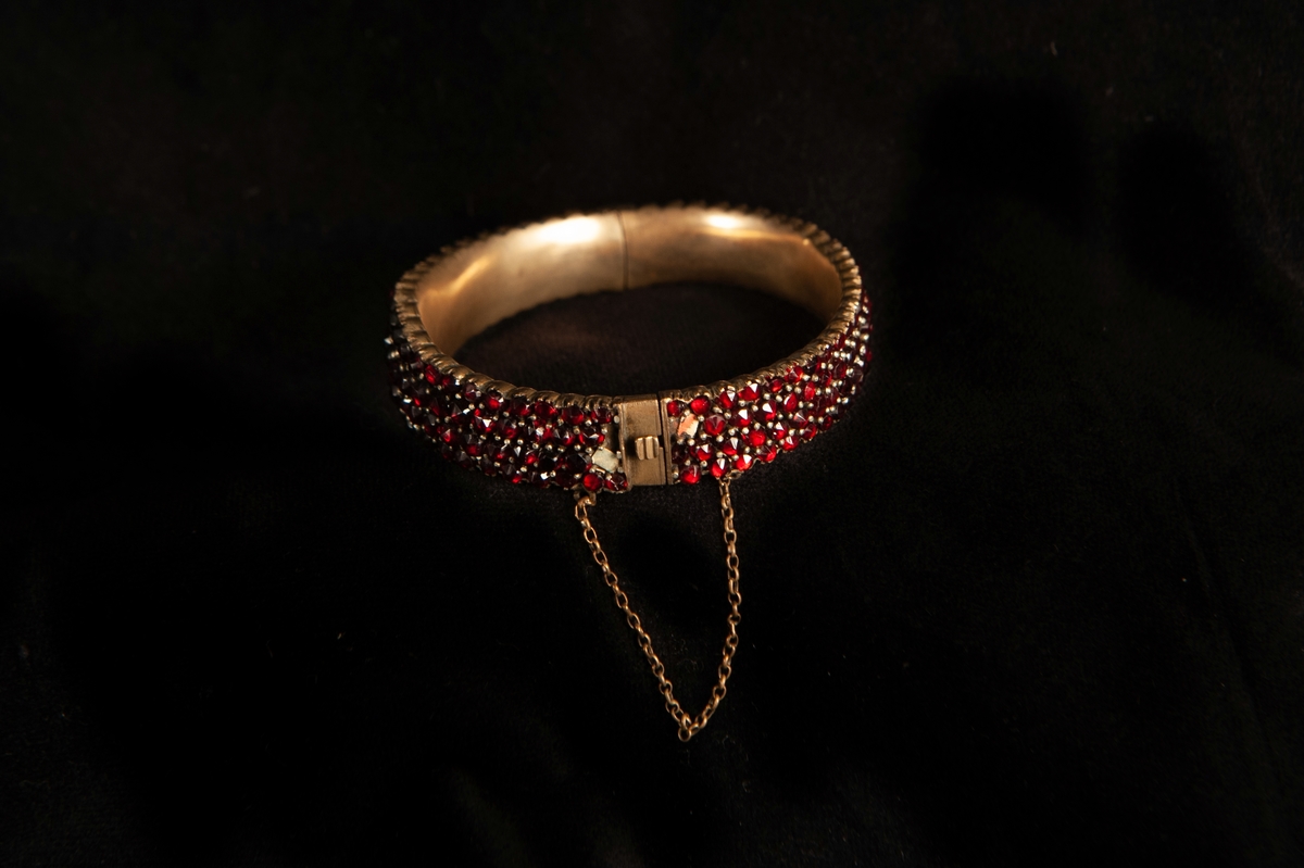 Ett armband, tätt besatt med slipade röda granater. Infattade i förgylld metall, troligen silver. Armbandet något avsmalnande åt sidorna.Smycket ligger i specialgjord svart, ask med röd sammet invändigt och ett snäpplås. 
Inga stämplar på armbandet.