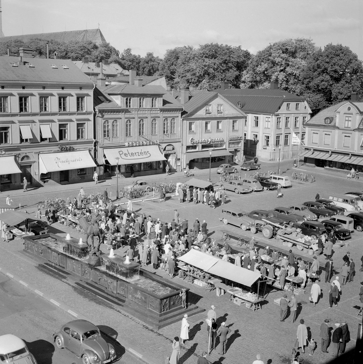 Vy över Stora torget i Linköping med pågående torghandel. Året är 1965 och ännu kan man behändigt parkera sin bil på torget.