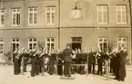 Göta livgardes musikkår ger konsert på kaserngården på Linnégatan, matsal och skolbyggnaden i bakgrunden.