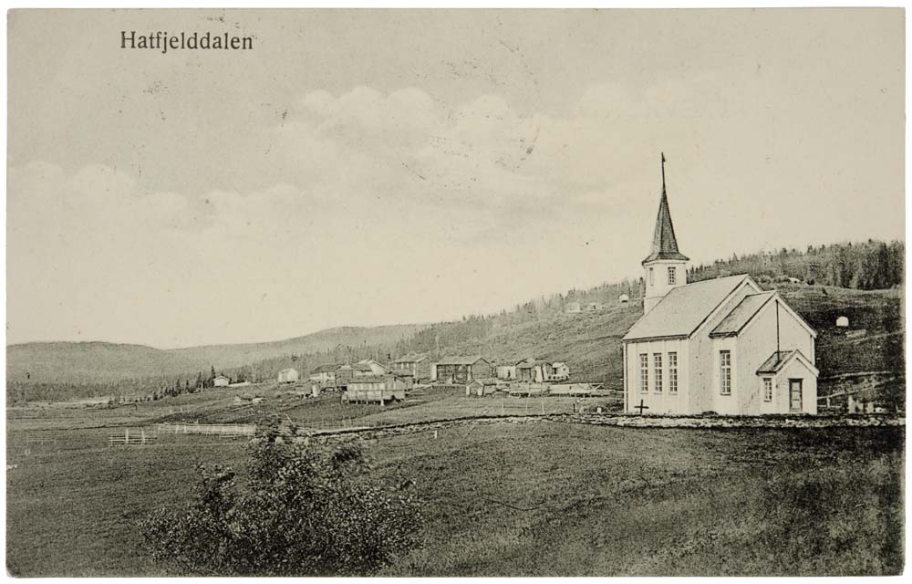 Postkort som viser Hattfjelldal kirke med bebyggelse.