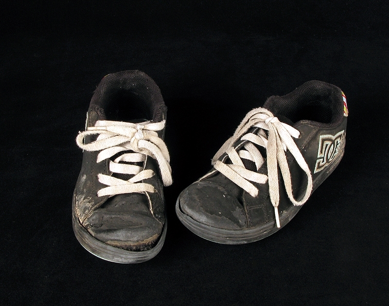 a) skateboardbräda av trä. Hjul saknas. Mått: längd 77,5 cm, bredd 19 cm, tjocklek 1 cm.
b1-b2) svarta skateskor. Märke: DC Shoe.
Märkning: "DCSHOECOUSA".
 Mått: längd 23 cm, bredd 9 cm, höjd 8,5 cm.
c1-c2) vita skateskor.  Märke: DC Shoe. 
Märkning: "DCSHOECOUSA". 
Mått: längd 22 cm, bredd 8, 5 cm, höjd 8,5 cm.