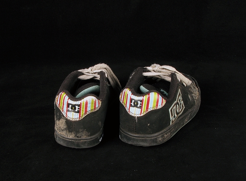 a) skateboardbräda av trä. Hjul saknas. Mått: längd 77,5 cm, bredd 19 cm, tjocklek 1 cm.
b1-b2) svarta skateskor. Märke: DC Shoe.
Märkning: "DCSHOECOUSA".
 Mått: längd 23 cm, bredd 9 cm, höjd 8,5 cm.
c1-c2) vita skateskor.  Märke: DC Shoe. 
Märkning: "DCSHOECOUSA". 
Mått: längd 22 cm, bredd 8, 5 cm, höjd 8,5 cm.