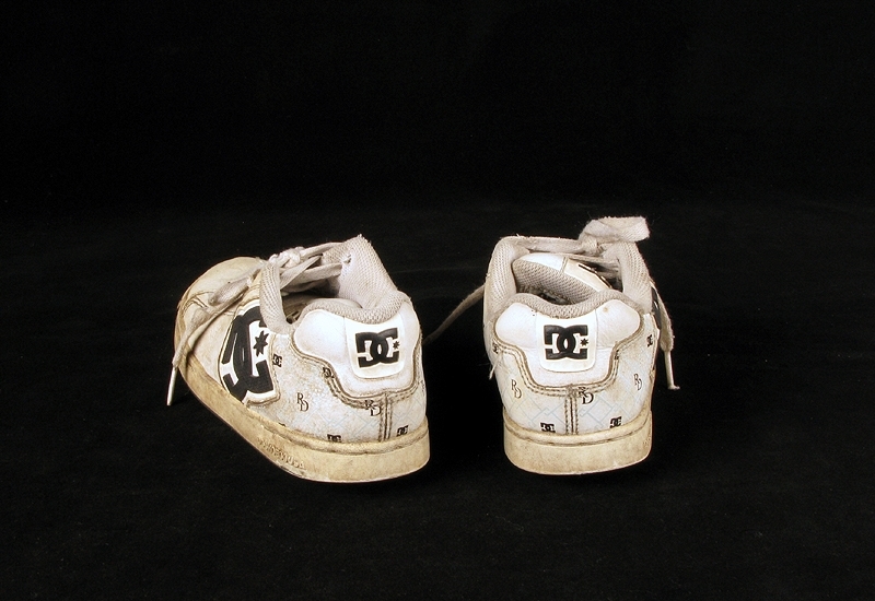 a) skateboardbräda av trä. Hjul saknas. Mått: längd 77,5 cm, bredd 19 cm, tjocklek 1 cm.
b1-b2) svarta skateskor. Märke: DC Shoe.
Märkning: "DCSHOECOUSA".
 Mått: längd 23 cm, bredd 9 cm, höjd 8,5 cm.
c1-c2) vita skateskor.  Märke: DC Shoe. 
Märkning: "DCSHOECOUSA". 
Mått: längd 22 cm, bredd 8, 5 cm, höjd 8,5 cm.