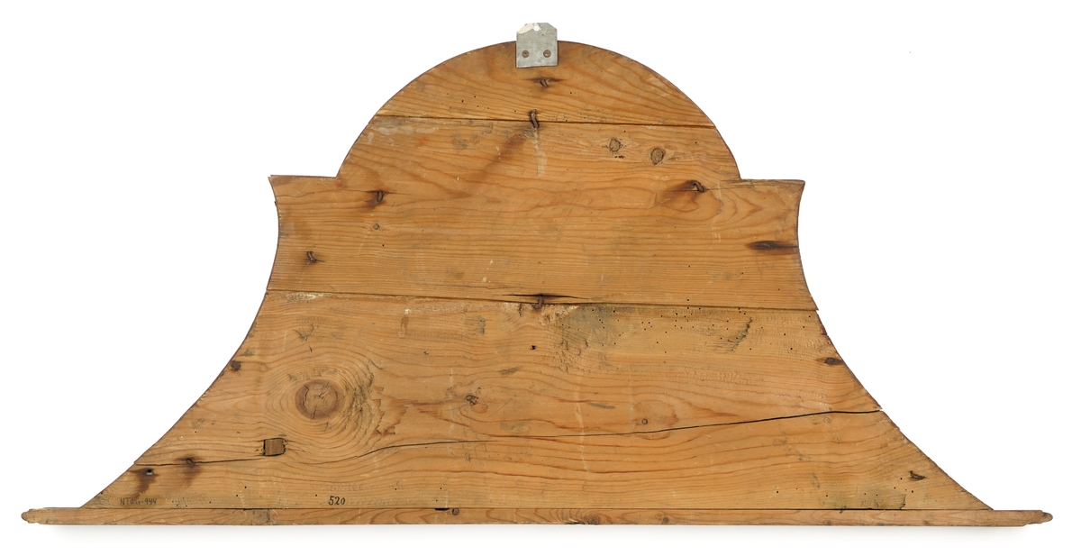 Døroverstykke bestående av 3 sammensatte trebord med not og fjær (bunnplaten). Trekantet med rett underkant, innadbuede sider og utadbuet overkant. Bunnplaten er utskåret og i flere nyanser av blått ,påsatt 2 forhøyninger. Den øverste er oval, blå med krone i gull og rødt over "CR" i brunt, langs kanten en lysutskåret bord. Den nederste er avlang, buet, blå med "Toldbetientens Contoir" skrevet med brunfarge. Langs kanten en lysutskåret bord, på hver side en lys,utskåret dusk. Skiltet omgitt av en rett list i underkant, en rød og grå buet,profilert list på sidene og i overkant.Tilhører et sett med tre døroverstykker .Jfr. B-bok nr. 518,519,520. Nr. 518 er borte (ToldCassererens Contoir") Antatt fra Christiania jfr. B-bok.