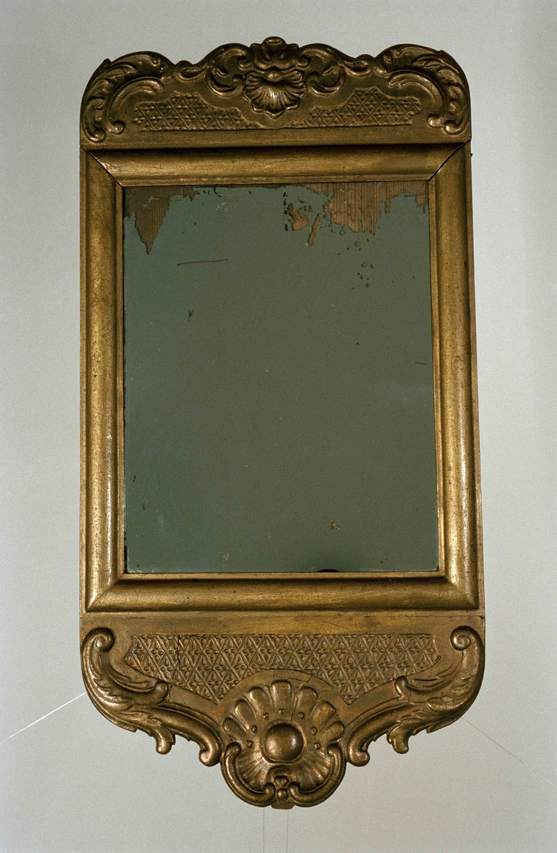 Spegel med skulpterad ram av barrträ, förgylld. Ramens över- och understycke med akantusblad och rocailler.