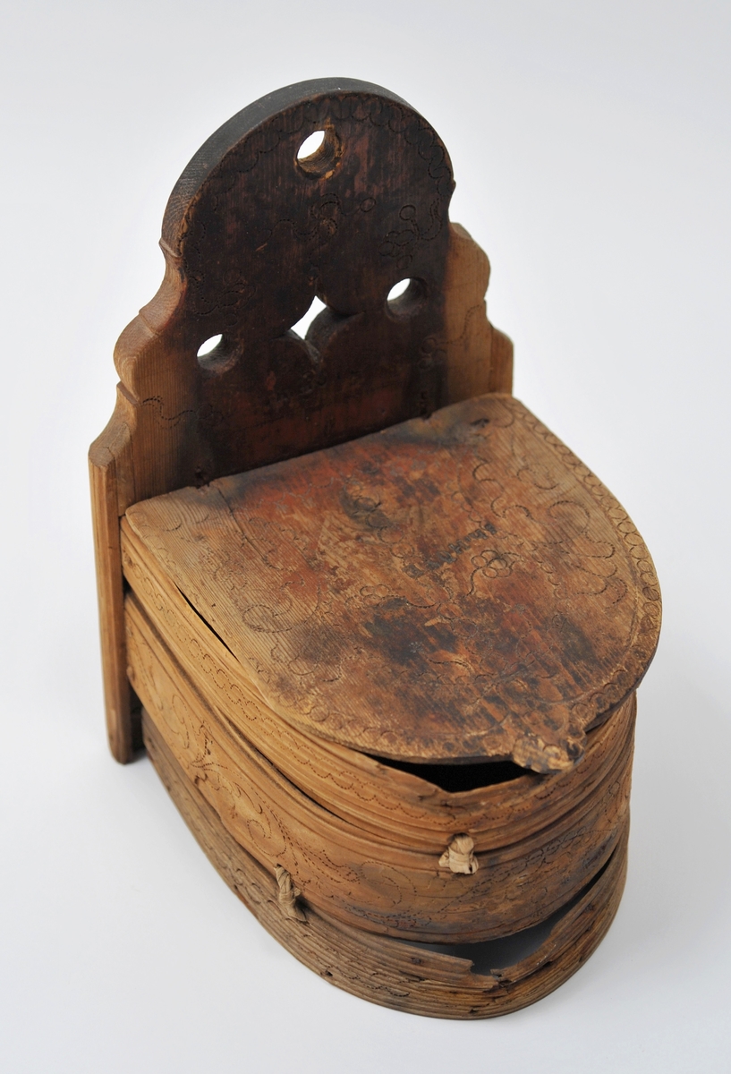 Sveipet laup med rett bakstykke, lagd for å kunne henges på en vegg, der den skulle henge som en beholder, opprinnelig sannsynligvis på et kjøkken. Sett rett ovenfra eller nedenfra er laupen formet som en halvoval. De veggene som skulle vende fram i rommet er lagd av tre forholdsvis tynne (7-8 millimeter) bjørkeskier, som er bøyd i en U-form. Endestykkene er festet i slisser langs kantene av bakstykket ved hjelp av trenagler. Disse tre komponentene er bundet sammen, kant mot kant ved hjelp av bindsler av trefibermateriale. Ytterflatene har svidekor - bølgemønstere på den øverste og nederste, og en akantusranke på den midtre, som er noe bredere enn de to andre. Bakstykket - ryggfjøla - er lagd av et 21,3 centimeter bredt og 1,9 centimeter tjukt (3/4-toms) bord, antakelig av granvirke. Det er vinkelrett avkuttet i den nedre enden, men overenden er avrundet og profilert. Her er det fire gjennbombrutte hull, hvorav tre er runde og det fjerde er firefliket. Det øverste av disse har vært brukt ved oppheng. Også denne delen av laupen har svidekor med elementer av de samme formene som finnes på veggenes forsider. På baksida er det innsvidd en ring, sammensatt av små sirkler, som omgir initialer og årstall: «KSS 1817». Forsida er svijernstemplet «Jh. HØYE». Laupen har et halvovalformet lokk, lagd av granvirke og prydet med et innsvidd mønster, bestående av sirkler, halvsirkler og akantusblader. Også her finner vi det nevnte svijernstempelet. Lokket og bakstykket kan se ut til å ha vært innsatt med et rødbrunt fargestoff. Opprinnelig hengsling mangler. Botnstykket mangler fullstendig, men et innfelt spor nederst på bakstykket og naglehull langs ytterkanten på den nederste buete skia antyder hvordan botnstykket har vært festet.