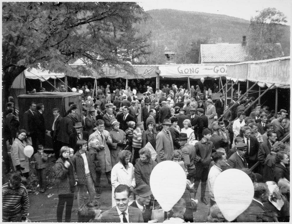 Masse folk på marked/tivoli med boder og ballonger.