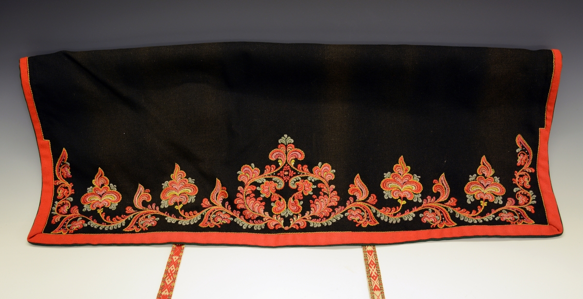 Modellbunad fra Vest-Telemark.TGM-BM.1999:0143.A-D.
B. Forkle. Sort forkle i ull med brodert bord i rosesøm nederst. Forkleet er kantet med et rødt og et grønt ullbånd. Påmontert forklebånd i grindvevteknikk i fargene rødt, hvitt, beige og grønt.