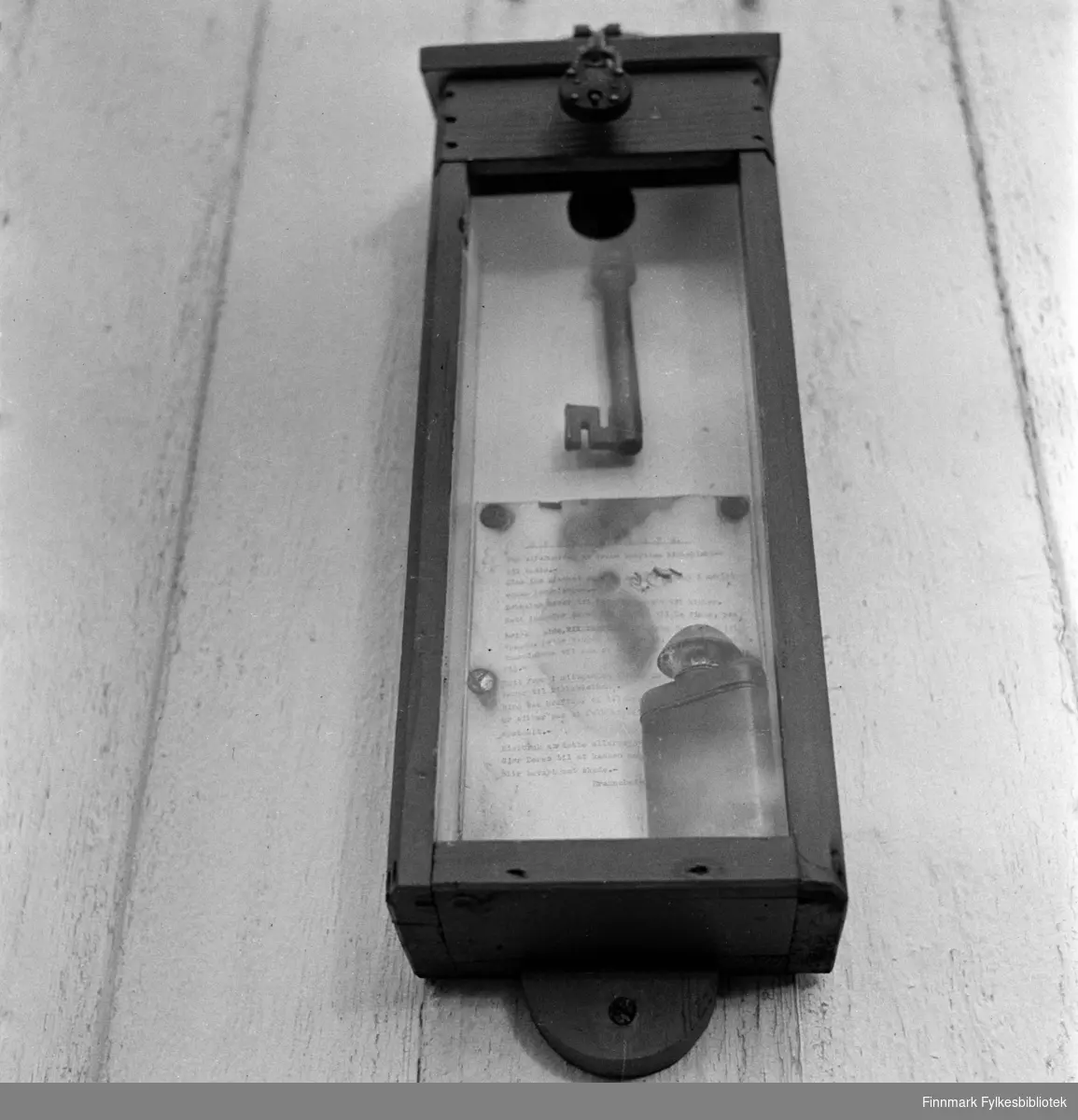 Kjøllefjord, 1940. Monter med kirkenøkkelen, instruksjoner for bruk samt en lommelykt. Hang i gamle Kjøllefjord kirke, sannsynligvis i våpenhuset. Interiøret i Kjøllefjord gamle kirke inneholdt blant annet en altertavle fra 1600-tallet. Kjøllefjord kirke var bygd i 1738 og sto i Kjøllefjord frem til den ble påtent av tyske soldater 4.november 1944 (Den brente jords taktikk). Kirken lå i Kjøllefjord prestegjeld som ble opprettet i 1685, da Skjøtningberg prestegjeld ble nedlat. Mye av inventaret stammet fra Skjøtningberg krike. Sakrestiet hadde en altertavle med årstallet 1662 som viser nattverdens innstiftelse. Denne skal tidligere å stått i Omgang kirke. Den opprinnelige kirken skal være byd mellom 1668 og 1683 og var en liten kirke bygget av rundtømmer. I kirken fantes også to klokker, hvorav den ene hadde inskripsjonen «Eine gude klock hin ick genant, den hört meinen klanck tho bargen int landt des late ick mi nicht vordreten. Heinrich Meier tho Bremen de oldermand he heft mi laten geten 1608. Restene av kirkeklokken kan ses i den nye Kjøllefjord kirke. Også den gotiske bibelen ble reddet av Hildur Hustad som tok med bibelen da hun flyktet til fjells. Bibelen oppbevares i dag i en bankboks i Kjøllefjord.