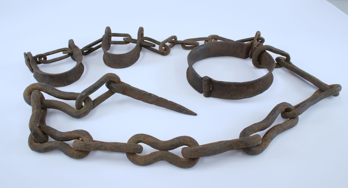 Halsjernet er hengslet og forsynt med "vinger" med gjennomgående hull for klinkenagle. (I dette hullet er det innsatt en skrue med mutter.) Lenke med 13 ledd er festet i halsjernet. Lenken ender i en sperre. Det er tredd to hesteskoformede fotjern på lenken. Fra halsringen er det festet en lenke med 11 ledd som ender i en kileformet bolt  med øye. Bolten er forsynt med mothaker for feste i trevegg.