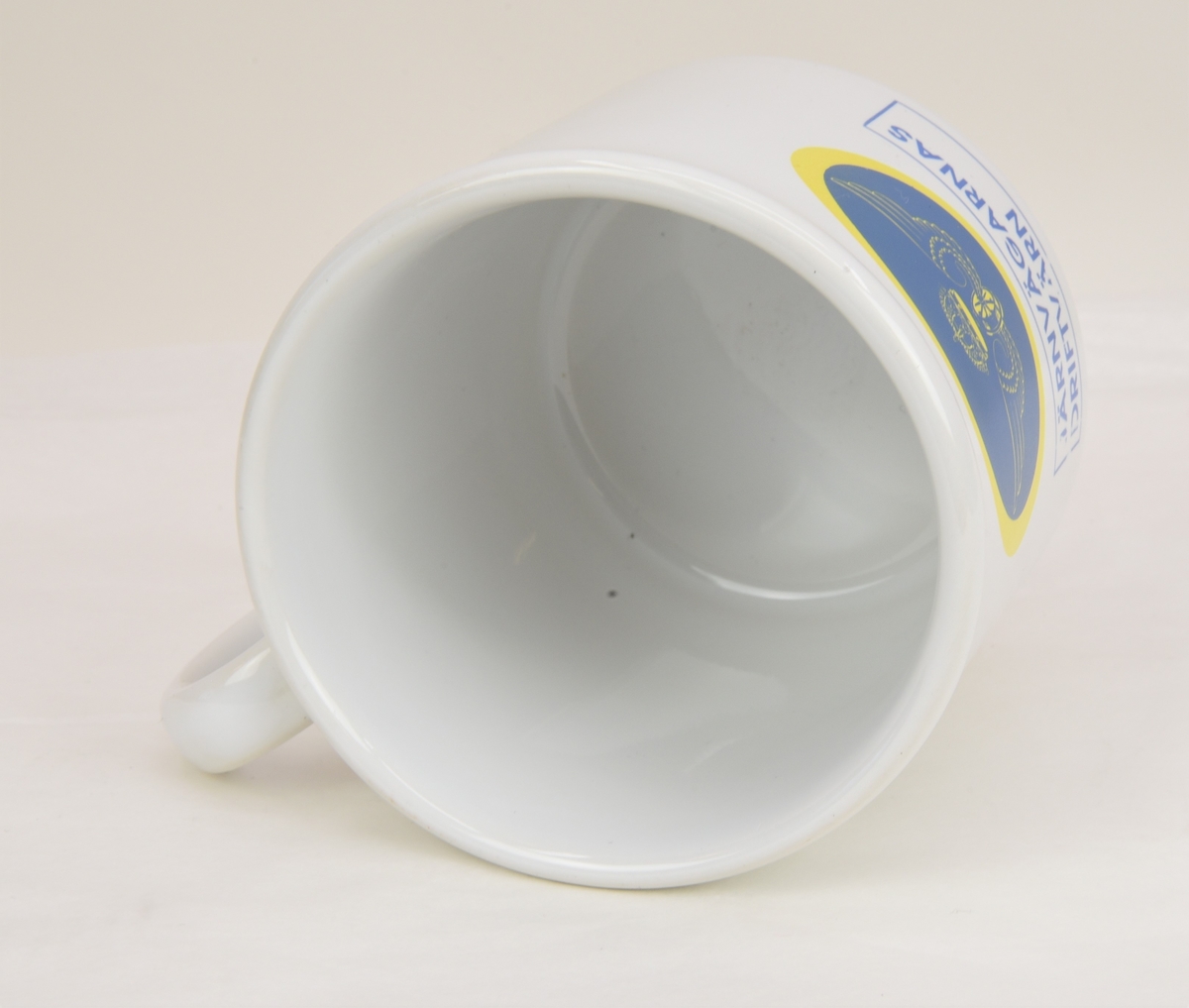 En vit kaffekopp av porslinmed tryckt motiv föreställande det bevingade samt krönta vinghjulet i en blå oval med gul kant. Nedanför texten "JÄRNVÄGARNAS DRIFTVÄRN" i en rektangel med en blå linje runtom.