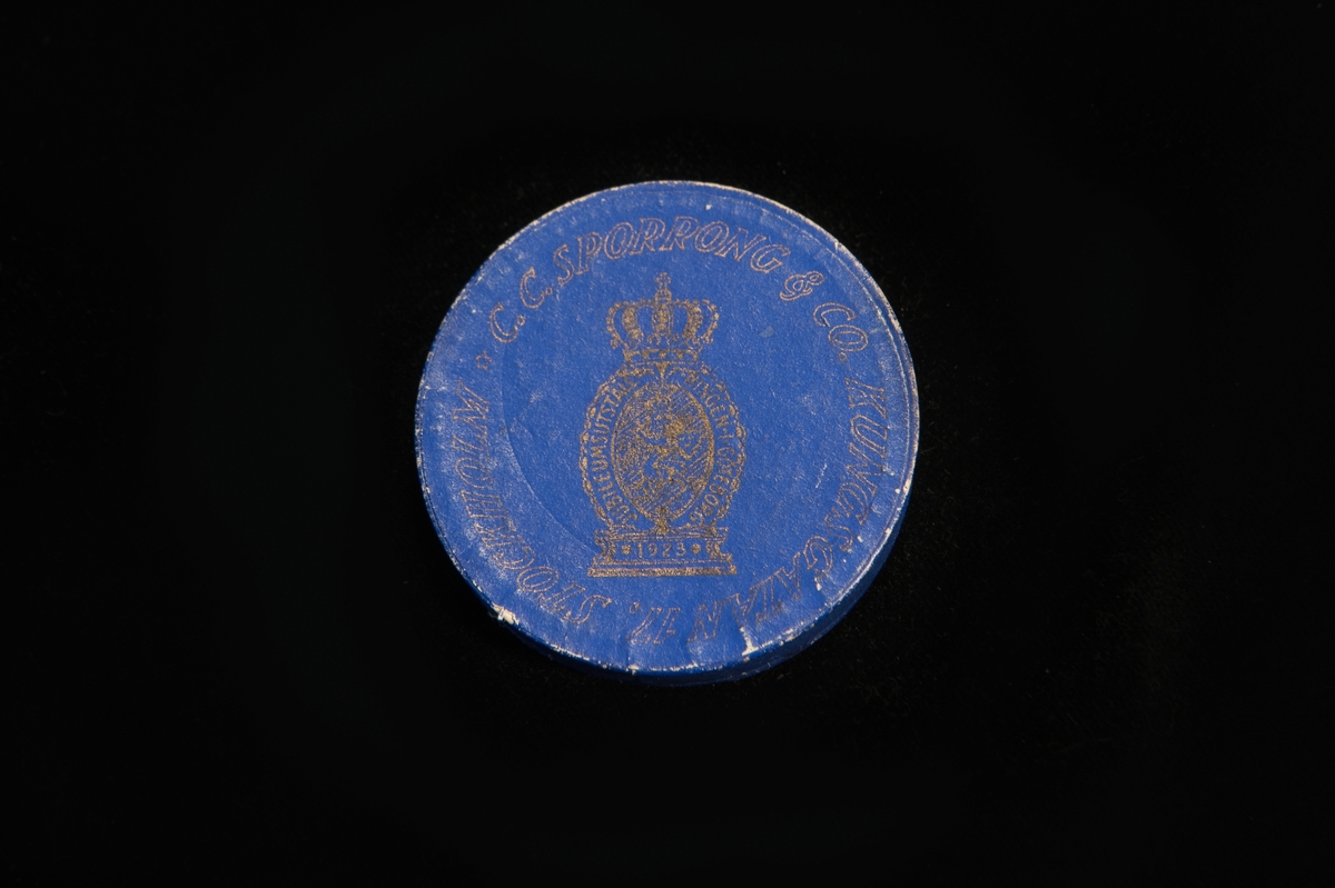 Utställningsmedalj av metall, förvarad i rund pappask klädd i blå papp med guldigt tryck på locket, "C.C. Sporrong  Co, kungsgatan 17, Stockholm". Även botten är tryckt med samma text i svart på beige botten.

Medaljens åtsida präglad med 4 persongestalter och en delfin, och frånsidan präglad med ett krönt lejon hållandes en sköld med tre kronor, samt texten "Jubileumsutställningen Göteborg" och årtalet 1923. Medaljkonstnär C. Milles.