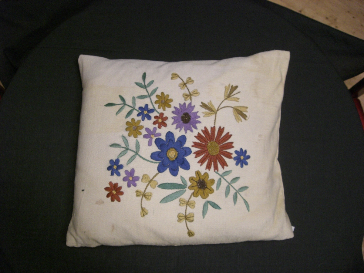 Sofapute med trekk i gult ullstoff, brodert blomstermotiver i plommefarget gult, grønt, blått og lilla bomullsgarn.
