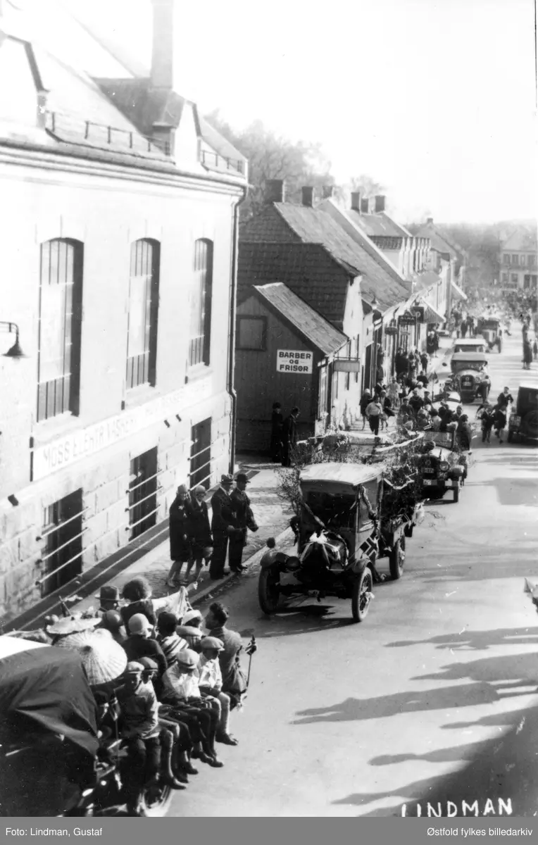 Postkort fra 17. mai-tog 1929 med bilkortesje, Storgata i Moss.  Moss Elektriske vaskeri til venstre. Og skilt for Barber og Frisør på veggen. En av bilene har kjennetegn B-27. B-27 står i Bilboken for Norge 1929 registrert på Ford lastebil, eier fru Bjørnstad, i Moss politidistrikt.