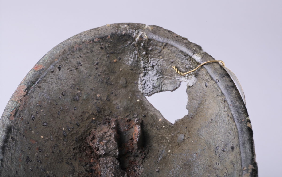 Oval bronsespenne med støpte ornamenter fra vikingtid. Variant av type Rygh 647. Funnet i en haug på gården Tråset i Fåberg i 1887.