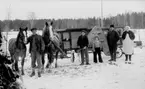 FEM PERSONER PÅ LADUGÅRDSBACKEN MED TVÅ HÄSTAR. 
DEN ENA HÄSTEN SPÄND FRAMFÖR ETT STORT TRÖSKVERK PÅ 
HJUL.