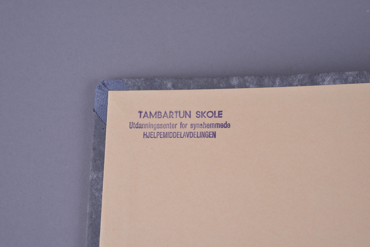 Innbundet bok med punktskrift. Tosidig trykk. Gråsvart omslag av kartong. Forsats av oransje papir. Sidene er av oransje papir. Tekstilhalvbind; ryggen og hjørnene er forsterket med rød tekstil. Sidene er heftet sammen ved hjelp av to meltallstenger som er festet til permene.