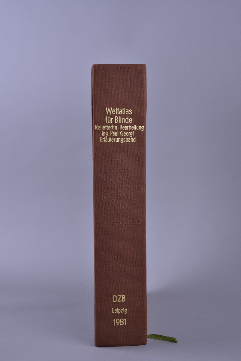 Innbundet bok med punktskrift. Tosidig trykk. Gråsvart omslag av kartong. Forsats av oransje papir. Sidene er av oransje papir. Tekstilhalvbind; ryggen og hjørnene er forsterket med rød tekstil. Sidene er heftet sammen ved hjelp av to meltallstenger som er festet til permene.
