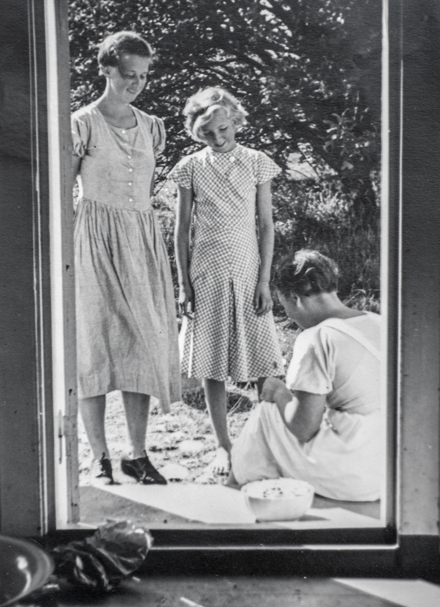 Aagot Sewell (f. Oos) sitjande i døropninga, søstrene Kirsti og Anne ståande. 