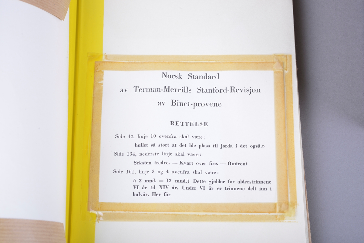 Rektangulær brun koffert av papp, med håndtak og lås. Inne i kofferten er det små pappesker. Pappeskene inneholder små treklosser, plater med pålimte miniatyr-leker. Blant annet dukke, hund seng, saks, pipe. I tillegg er det flere små knapper, notatblokk og tekstilbånd. I kofferten ligger også en bok merket "TERMAN-MERRILL // NORSK STANDARD".