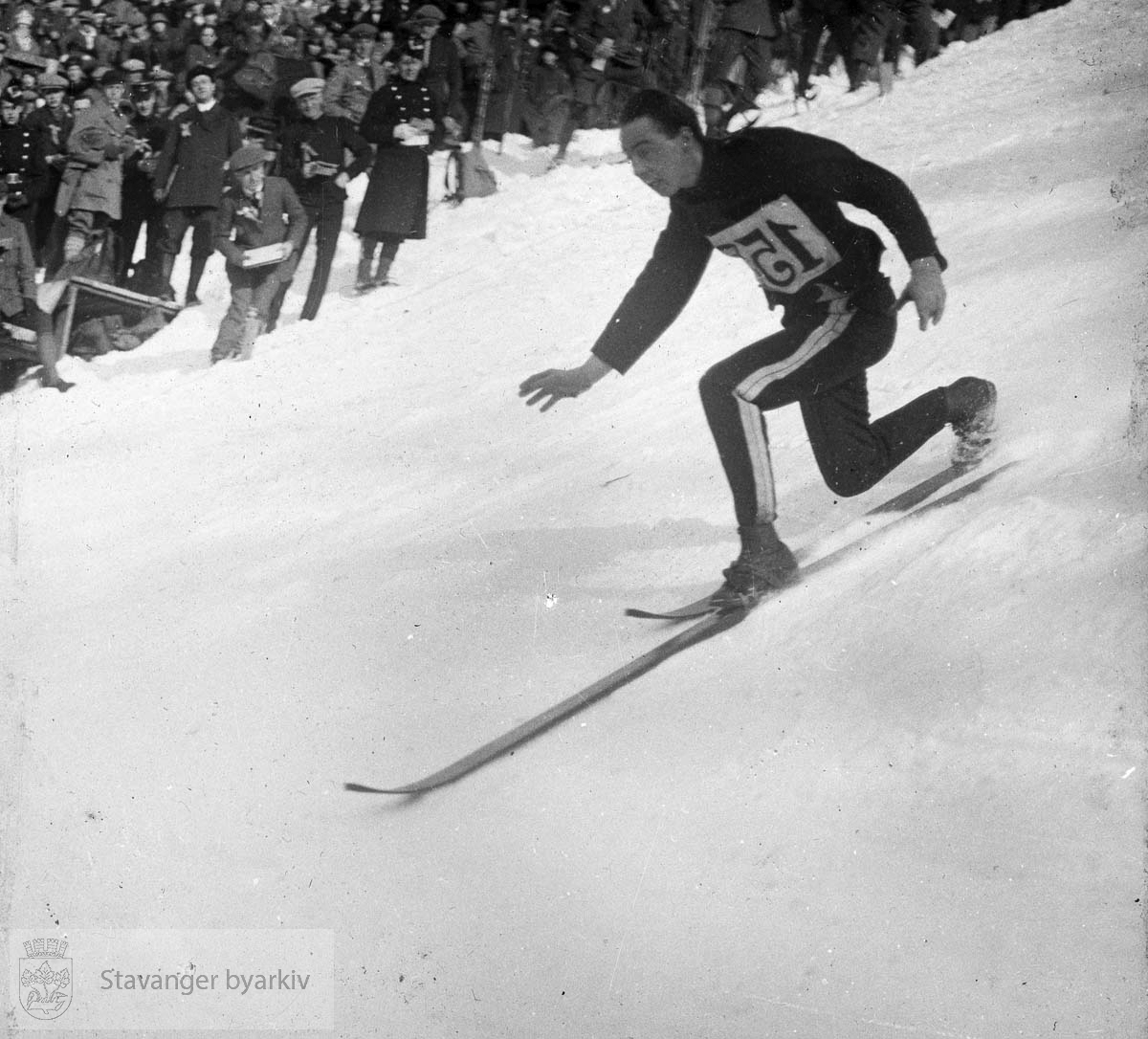 Enten skihopper som gjør nedslag, eller telemarkskjøring. Publikum i bakgrunnen......Arkivene til Gard Paulsen og Hans Henriksen ble avlevert sammen. Det er dermed noe usikkert hvem som egentlig er fotograf. Enkelte bilder kan ha blandet seg.