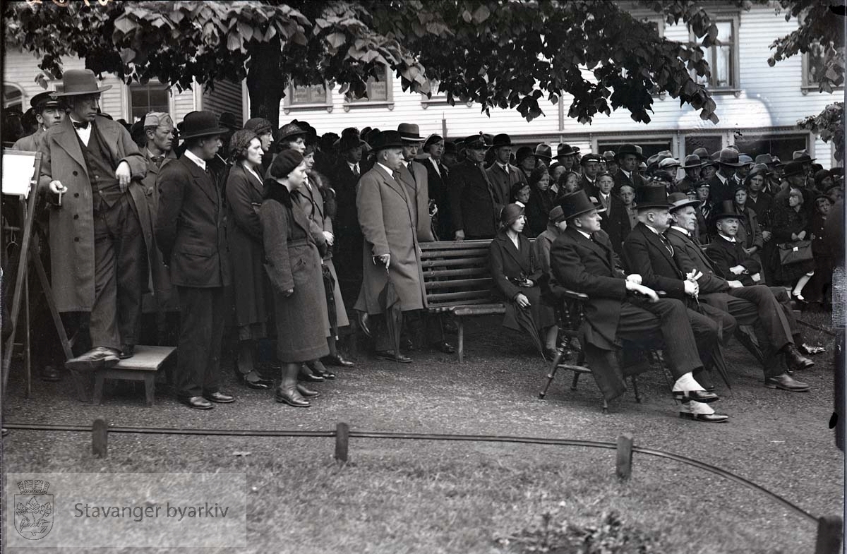 Tilskuerer samlet i parken. L.W. Hansen (?) og Bertram C. Middelthon sittende på benken til høyre. Kommunebiblioteket i bakgrunnen.