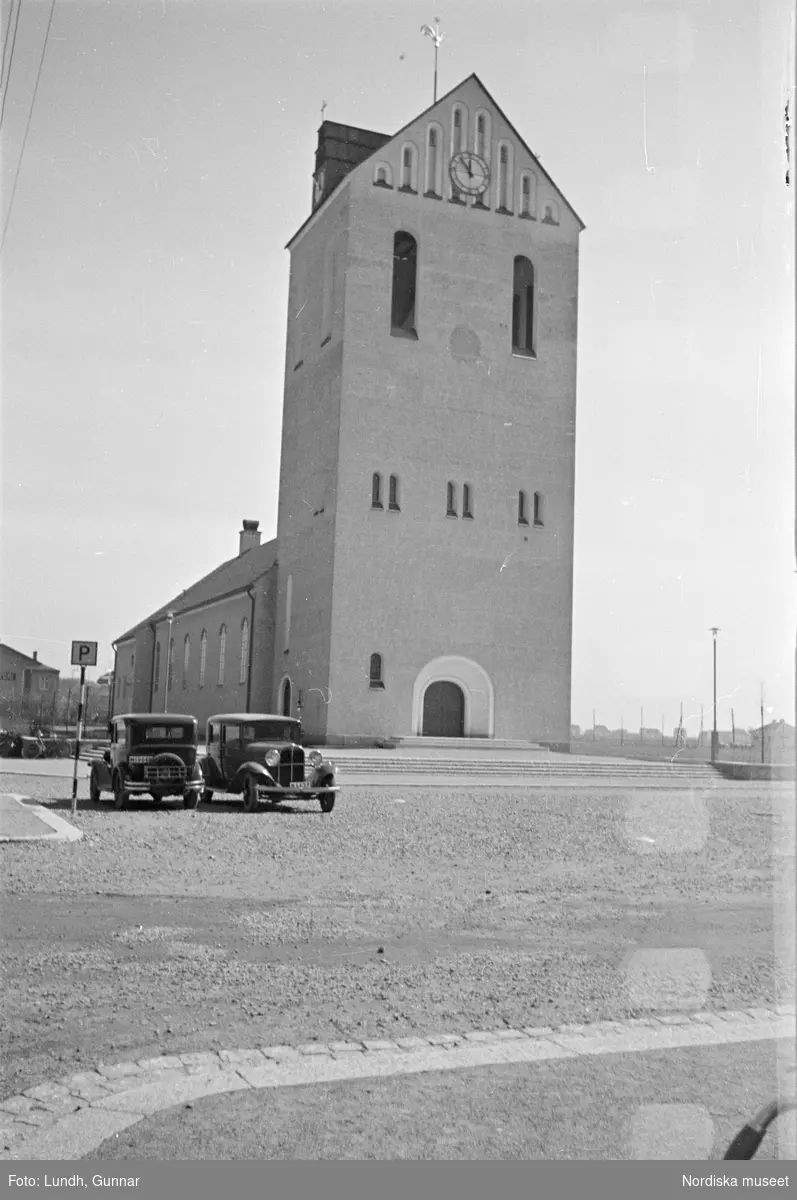 Exteriör av Höganäs kyrka, Himmelfärdskyrkan, under byggnation och som nybyggd, en kyrkobyggnad omgiven av byggnadsställningar, två bilar parkerade framför en kyrka.