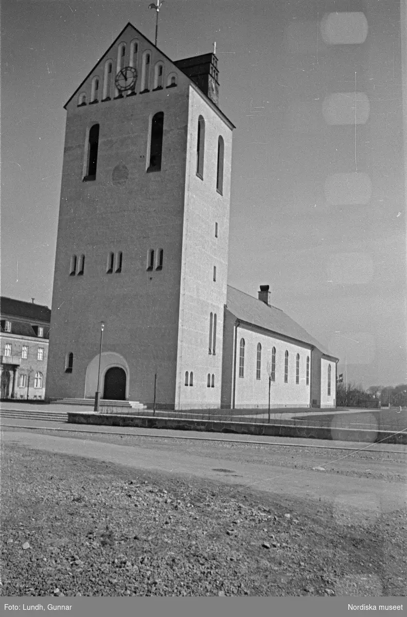 Exteriör av Höganäs kyrka, Himmelfärdskyrkan, under byggnation och som nybyggd, en kyrkobyggnad omgiven av byggnadsställningar, två bilar parkerade framför en kyrka.