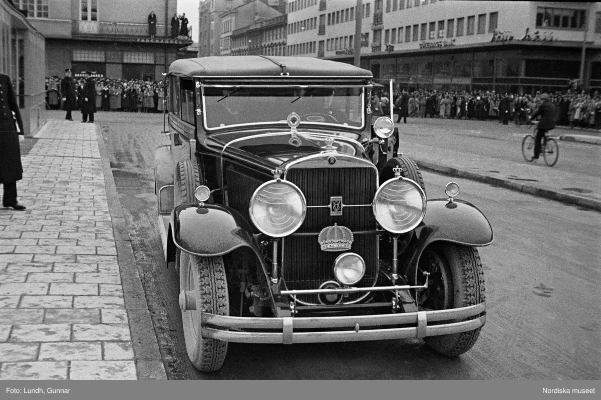 Invigning av Södra Bantorgets (Medborgarplatsen) tunnelbanestation på Södertunneln den 30 september år 1933, Kung Gustaf V kliver in i en bil, porträtt av en man i uniform - en chaufför vid Kungliga Hovstallet, detalj av en bil med lykta och skärm, en grupp män går ut ur en tunnelbanenedgång på Södra Bantorget - män i uniform gör honnör och i bakgrunden står människor i öppna fönster.