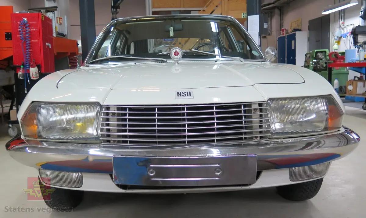 NSU RO 80. 4-dørs hvit bil med brunt interiør. Bilen har en bensindrevet dobbel NSU/Wankel rotasjonsstempelmotor, med sylindervolum på 994 kubikkcentimeter (cm3), og effekt på 115 DIN HK. Dekkdimensjon foran og bak skal standard være 175 HR 14. Framhjulstrekk. Girkasse med 3 gir framover pluss revers. Kilometerstand er 75385.