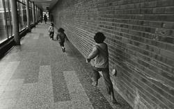Barn springer efter varandra i lång korridor med tegelvägg p