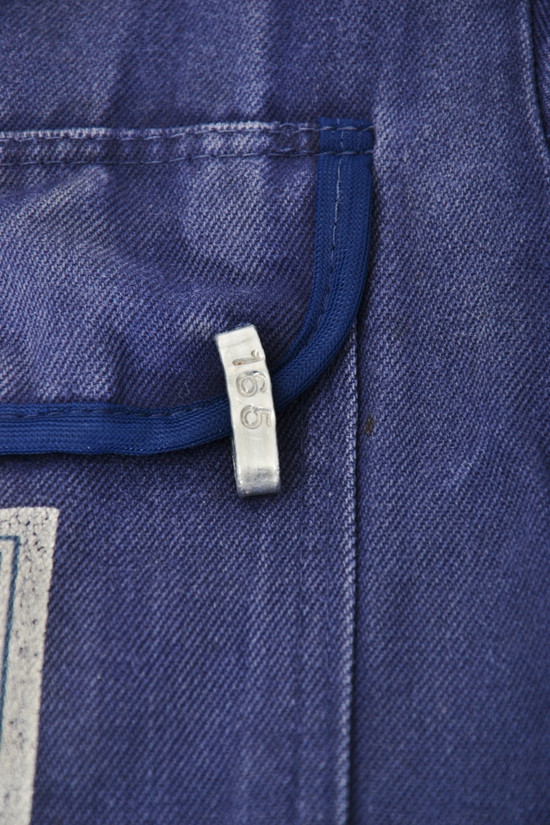 Blå bomullskjeledress i størrelse 56 med logo på venstre brystlomme. Lukking med metallknapper. To brystlommer og to stikklommer i front og to baklommer og strikk i ryggen.  
Logoen er utformet som et kvadrat med hvit bunnfarge og bokstavene ESN i rødt øverst og et stilisert blått anker under.
Kjeledressen har et metallmerke i venstre brystlomme - nr. 165; brukers arbeidsnummer - som var viktig i forbindelse med vask av arbeidstøyet.