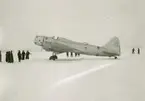 Sovjetiskt flygplan Iljushin DB-3 står på ett fält under finska vinterkriget, 1940. Människor i rörelse runtomkring. Bild från F 19, Svenska frivilligkåren i Finland.