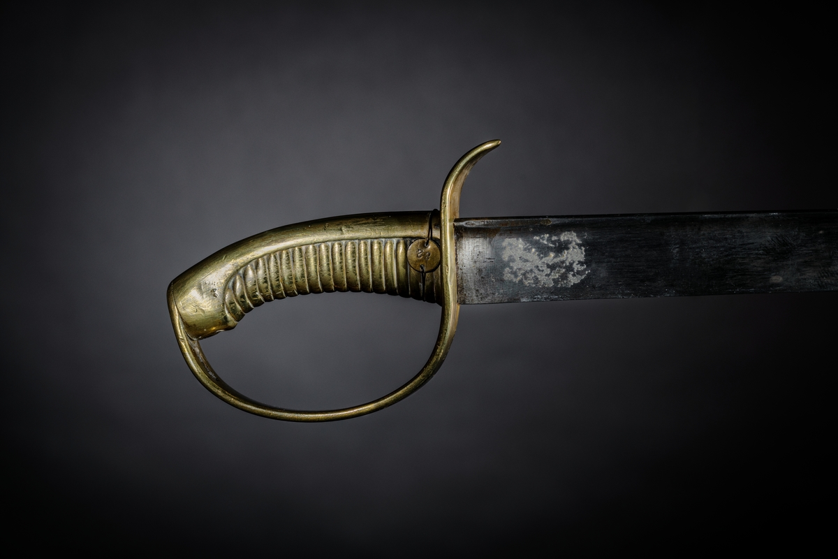 Huggare m/1846 för skeppsgossekåren med eneggad klinga av stål, Hafströms konstruktion. Fäste helt i mässing med räfflad kavel och parerstång som övergår i handbygel. Märkt : "1:C 86" instansat på parerstången, samt "82" instansat på en liten rund mässingsbricka, fästad med mässingstråd runt kaveln.