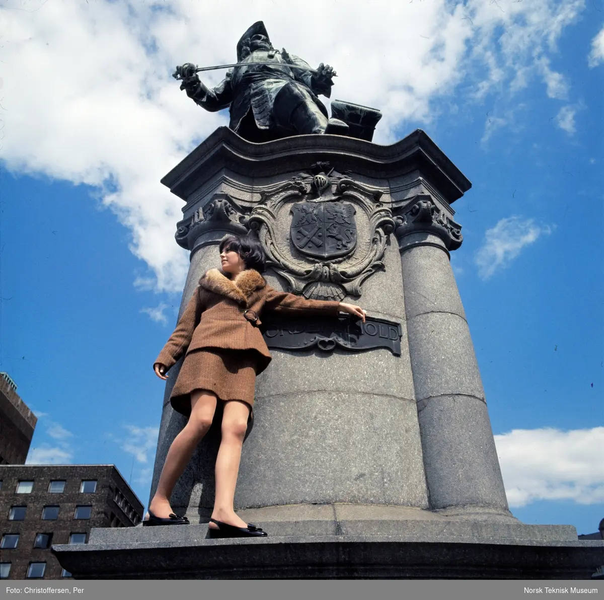 Motebilde i farger. Kvinnelig modell i todelt brun ulldrakt med pelskrage, foran statuen av Peter Wessel Tordenskiold (1901) av Aksel Ender på Rolf Strangers plass/ Rådhusplassen i Oslo, 1968. Bildet er en del av en serie der noen er publisert i en motereportasje i ukebladet Det Nye samme høst.