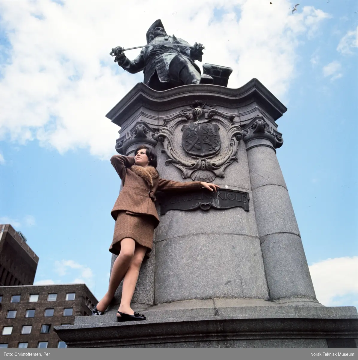 Motebilde i farger. Kvinnelig modell i todelt brun ulldrakt med pelskrage, foran statuen av Peter Wessel Tordenskiold (1901) av Aksel Ender på Rolf Strangers plass/ Rådhusplassen i Oslo, 1968. Bildet er en del av en serie der noen er publisert i en motereportasje i ukebladet Det Nye samme høst.