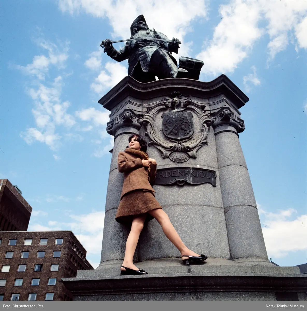 Motebilde i farger. Kvinnelig modell i todelt brun ulldrakt med pelskrage, foran statuen av Peter Wessel Tordenskiold (1901) av Aksel Ender på Rolf Strangers plass/ Rådhusplassen i Oslo, 1968. Bildet er en del av en serie der noen er publisert i en motereportasje i ukebladet Det Nye samme høst.